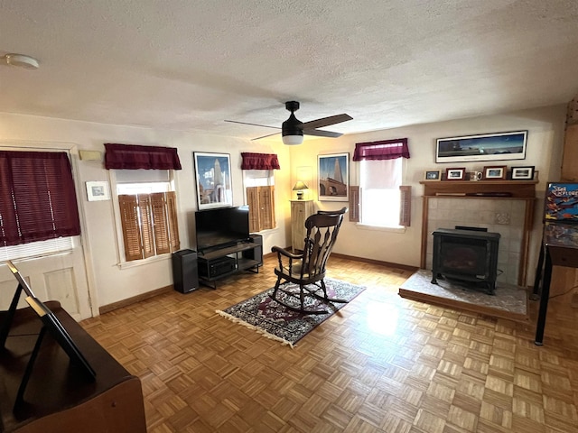 living room with ceiling fan, a wood stove, baseboards, and a textured ceiling