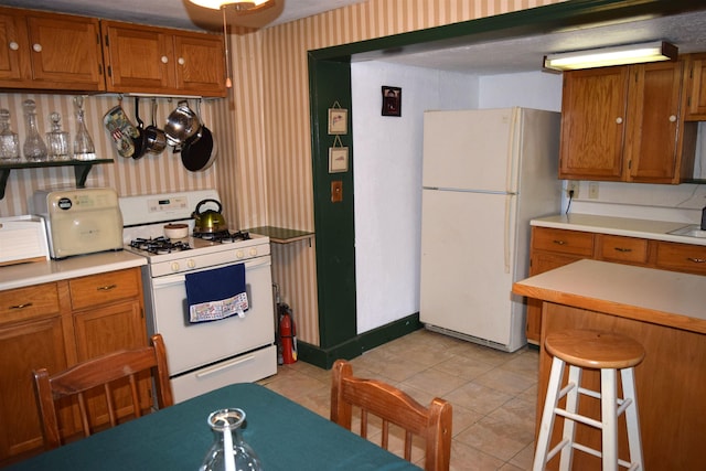 kitchen featuring white appliances, light countertops, brown cabinetry, and wallpapered walls