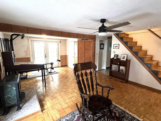 sitting room featuring stairway, french doors, a wood stove, a textured ceiling, and a ceiling fan