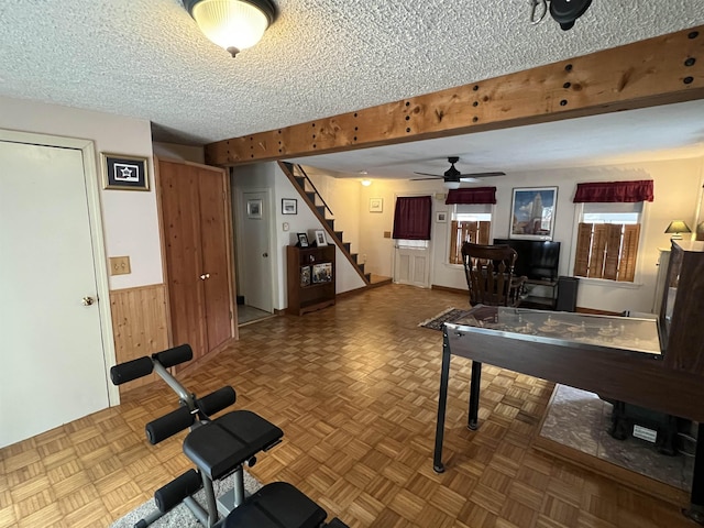 playroom with wooden walls, beamed ceiling, a wainscoted wall, and a textured ceiling