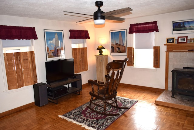 living area featuring a ceiling fan, baseboards, a textured ceiling, and a wood stove