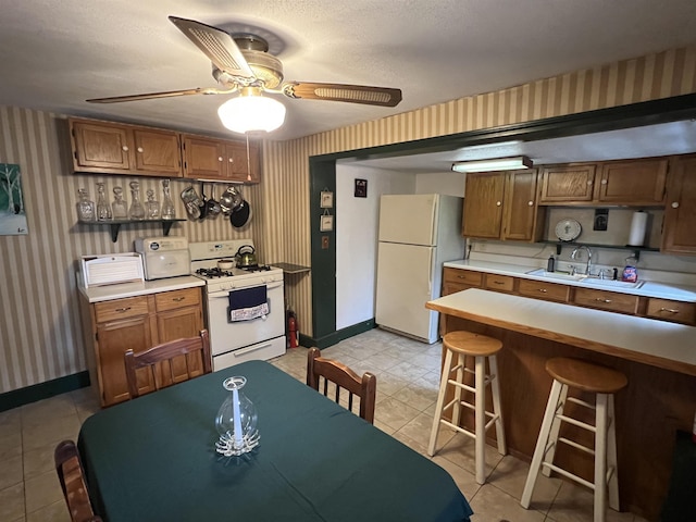 kitchen with white appliances, wallpapered walls, baseboards, and a sink