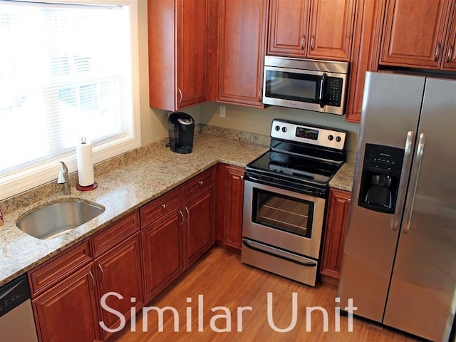 kitchen with a sink, stainless steel appliances, light stone counters, and light wood-style flooring