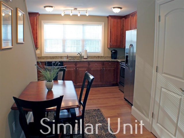 kitchen featuring light wood finished floors, appliances with stainless steel finishes, brown cabinetry, stone countertops, and a sink