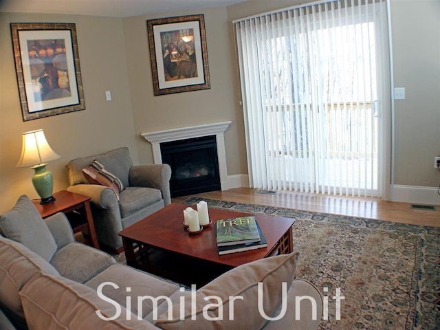 living room with visible vents, a fireplace, baseboards, and wood finished floors