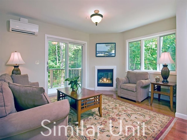 living area with a glass covered fireplace, wood finished floors, and a wall mounted AC