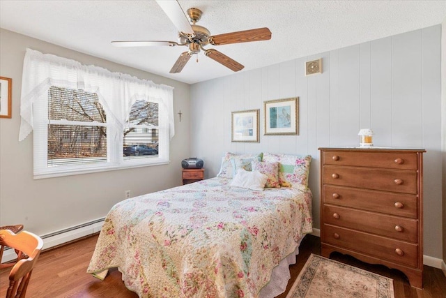 bedroom with ceiling fan, a baseboard heating unit, a textured ceiling, and wood finished floors