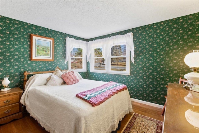 bedroom with baseboards, a textured ceiling, wood finished floors, and wallpapered walls