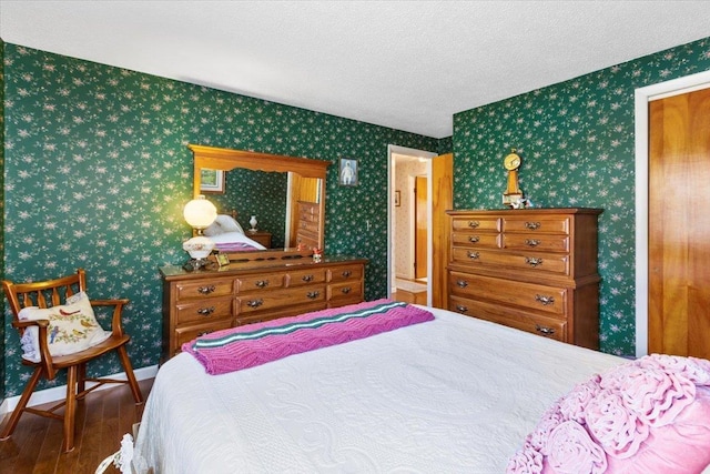 bedroom with baseboards, a textured ceiling, wood finished floors, and wallpapered walls