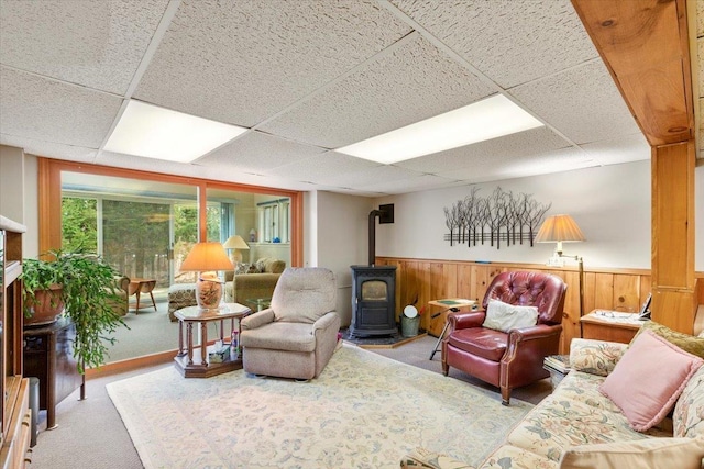 carpeted living area featuring a wood stove, a wainscoted wall, a drop ceiling, and wood walls