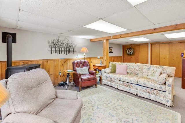 living room featuring a wood stove, a paneled ceiling, wooden walls, and wainscoting