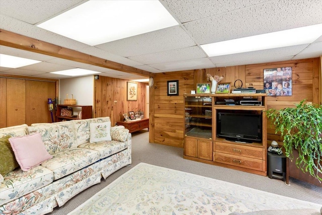 carpeted living room with wooden walls and a drop ceiling