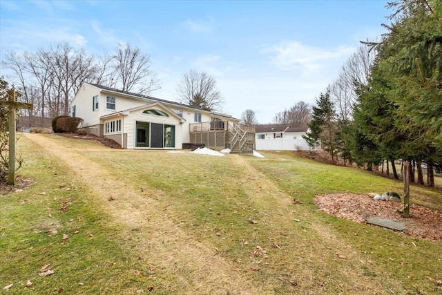 rear view of property with a yard, dirt driveway, a deck, and stairs