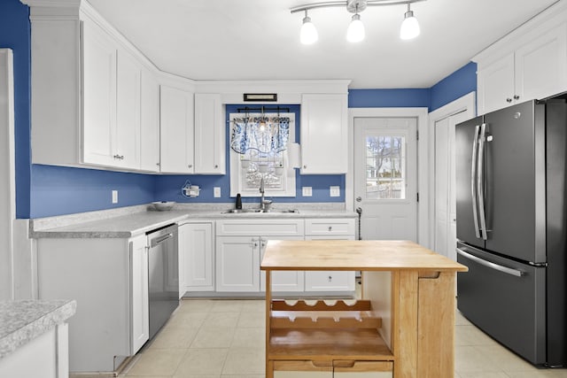 kitchen with a sink, stainless steel appliances, light tile patterned flooring, and white cabinets