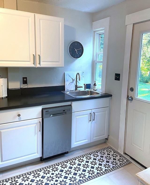 kitchen featuring stainless steel dishwasher, dark countertops, white cabinets, and a sink