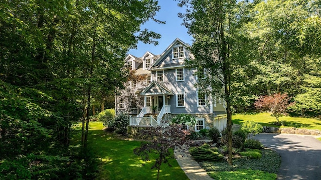 shingle-style home featuring aphalt driveway, stone siding, an attached garage, and a front yard