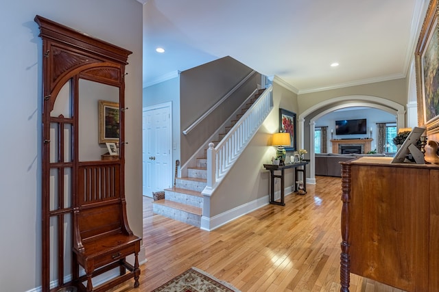 interior space featuring crown molding, baseboards, stairs, a fireplace, and light wood-style floors