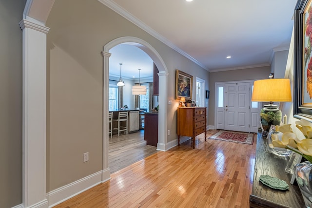 foyer entrance with crown molding, light wood-style floors, arched walkways, and ornate columns