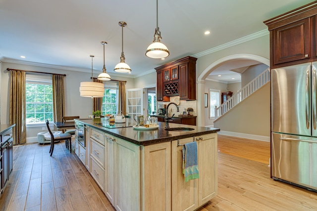 kitchen featuring light wood-type flooring, a kitchen island with sink, a sink, tasteful backsplash, and freestanding refrigerator