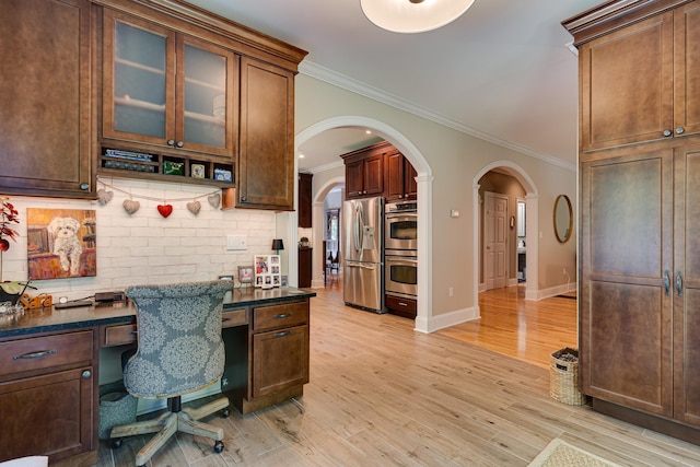 office area featuring arched walkways, light wood finished floors, built in study area, and crown molding