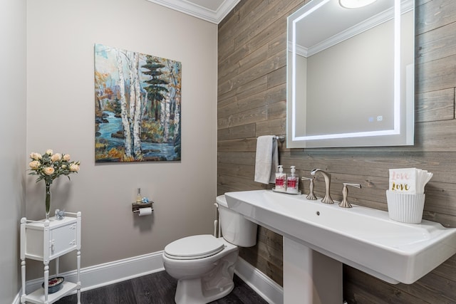 bathroom featuring wooden walls, crown molding, baseboards, toilet, and wood finished floors