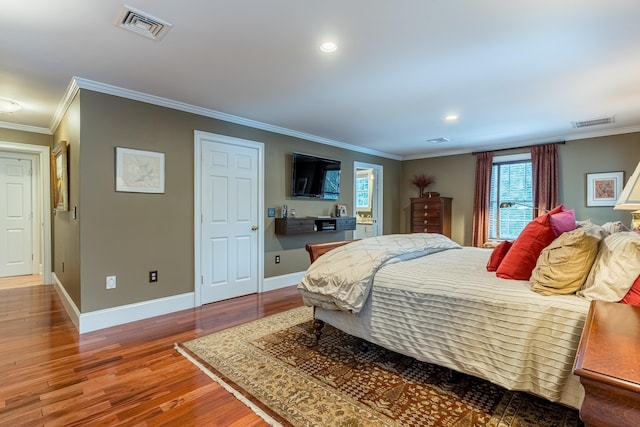 bedroom featuring visible vents, baseboards, wood finished floors, and crown molding