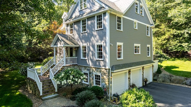 view of front of home with stone siding, driveway, a shingled roof, and a garage