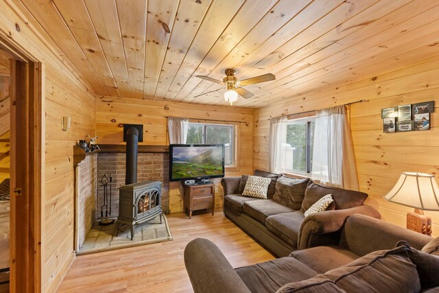 living room with wood walls, wooden ceiling, light wood finished floors, ceiling fan, and a wood stove