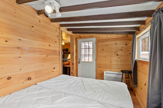 bedroom featuring beam ceiling, wood walls, and wood finished floors