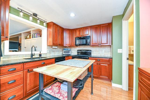 kitchen featuring dark stone countertops, light wood-style flooring, a sink, black appliances, and backsplash