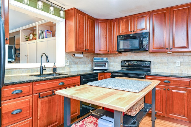 kitchen with light wood finished floors, dark stone counters, a sink, decorative backsplash, and black appliances