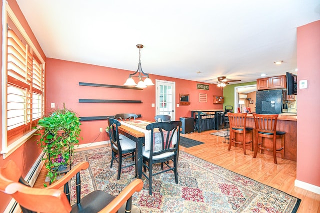 dining room with a healthy amount of sunlight, ceiling fan with notable chandelier, light wood-type flooring, and baseboards