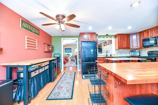 kitchen with light wood finished floors, wooden counters, a breakfast bar area, black appliances, and a sink