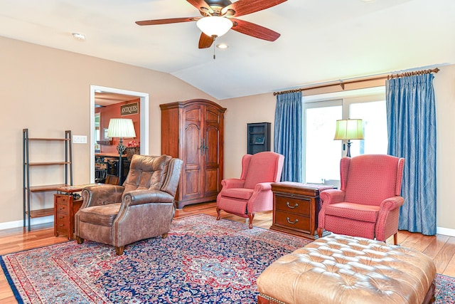 living area featuring baseboards, lofted ceiling, light wood-style floors, and a ceiling fan