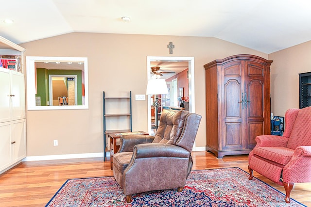 living area with baseboards, light wood-style flooring, and vaulted ceiling