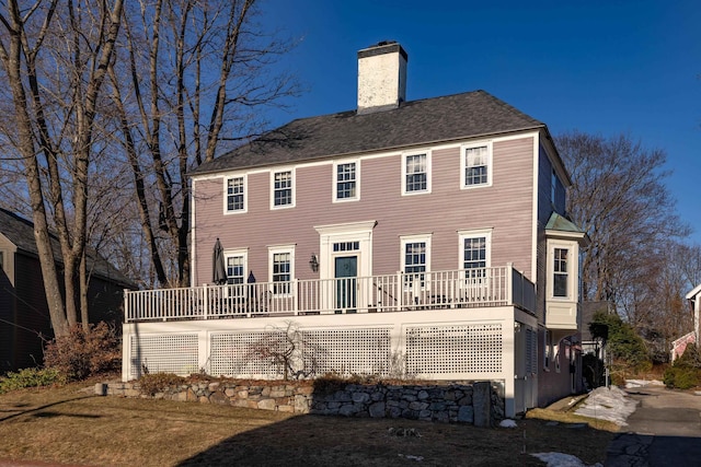 back of house with a chimney and a shingled roof