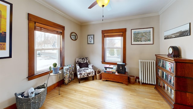 sitting room with crown molding, radiator heating unit, a ceiling fan, and wood-type flooring