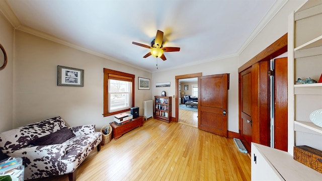 sitting room featuring light wood-type flooring, ceiling fan, radiator heating unit, and crown molding