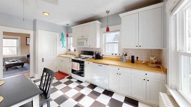 kitchen featuring white appliances, radiator, hanging light fixtures, decorative backsplash, and tile patterned floors