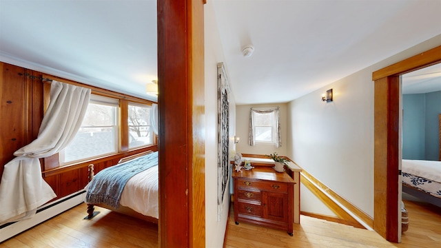 bedroom with light wood-type flooring, a baseboard heating unit, and baseboards