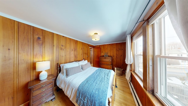 bedroom with wooden walls, a baseboard heating unit, and light wood-type flooring