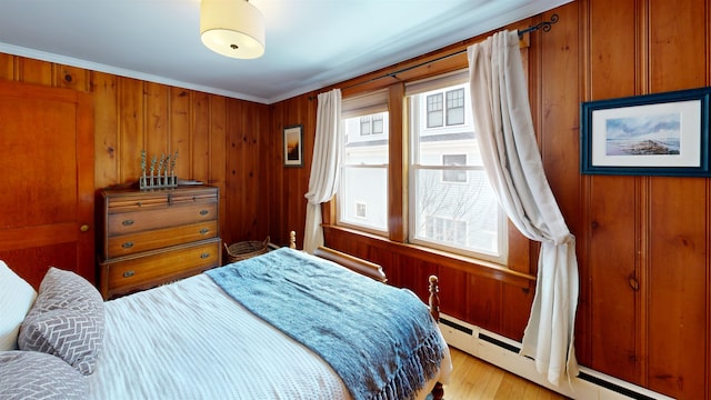 bedroom with baseboard heating, multiple windows, light wood-style flooring, and ornamental molding