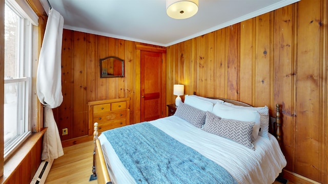 bedroom featuring light wood finished floors, wooden walls, baseboards, and ornamental molding