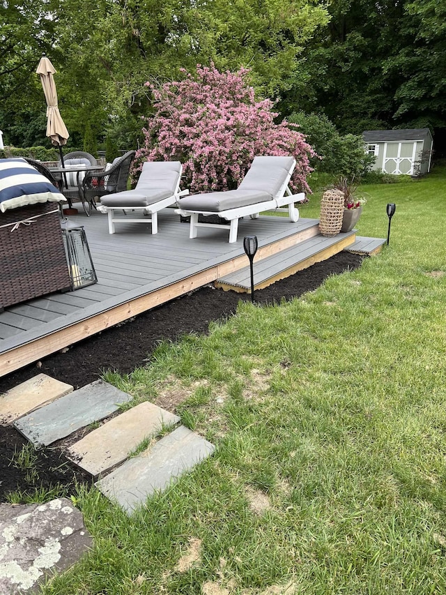 deck featuring a storage unit, a lawn, an outdoor structure, and outdoor dining space