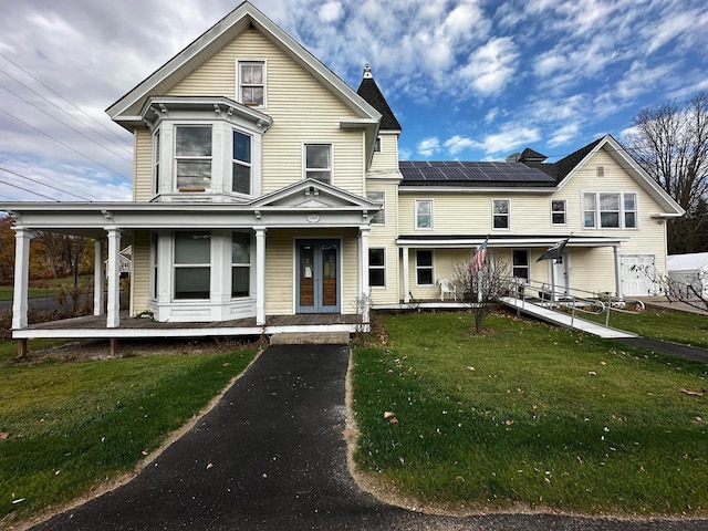 view of front of property with solar panels, a front yard, and covered porch