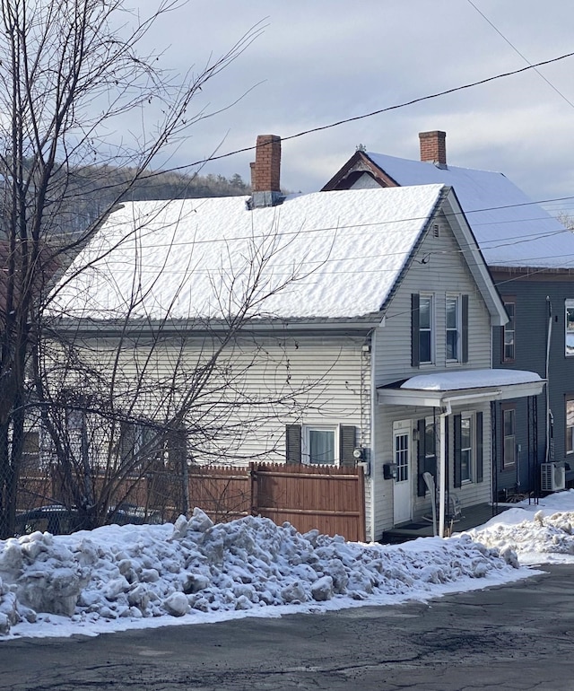 view of front of house featuring central air condition unit, covered porch, a chimney, and fence