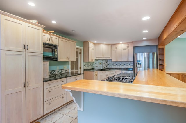 kitchen with butcher block countertops, a sink, light tile patterned flooring, stainless steel fridge with ice dispenser, and black microwave