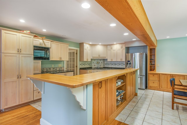 kitchen with a sink, wood counters, a center island, stainless steel fridge, and black microwave