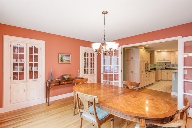 dining room with light wood-style flooring, a notable chandelier, and baseboards