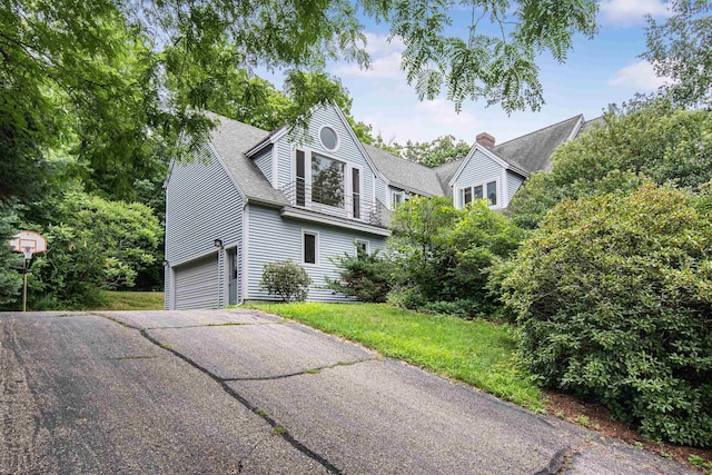 view of front of house with aphalt driveway, a front yard, a shingled roof, a garage, and a chimney